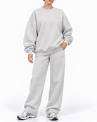 A woman modeling a light gray heather crewneck sweatshirt and matching sweatpants set, paired with gray and white sneakers, against a plain white studio background.