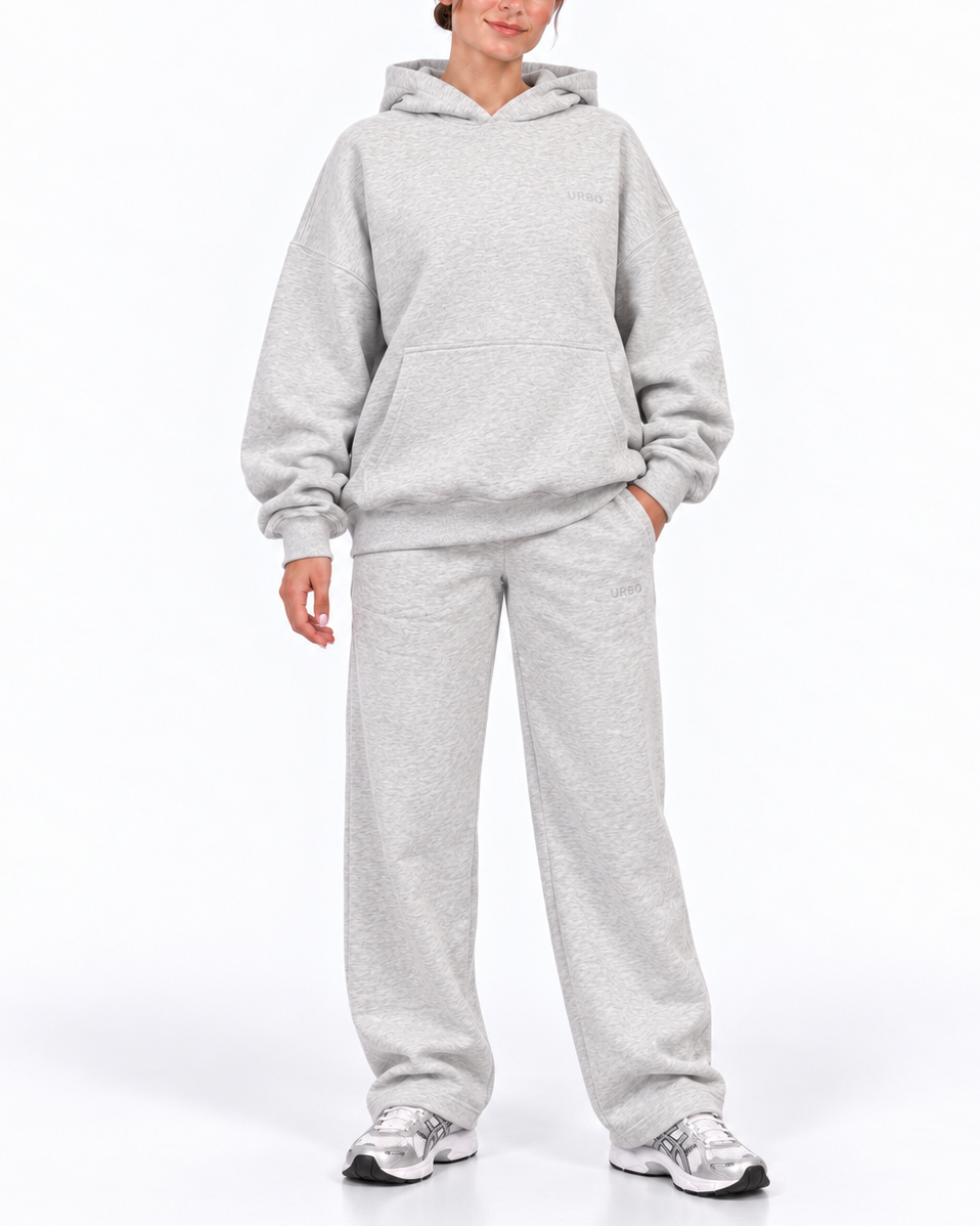 A woman modeling a light gray heathered hooded sweatshirt and matching sweatpants set, standing against a clean white studio background.