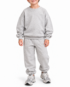 A young boy wearing a light gray heather sweatshirt and matching sweatpants with gray sneakers, standing against a plain white background.