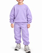 A young boy wearing a matching lavender sweatshirt and jogger pants set, standing against a plain white background.