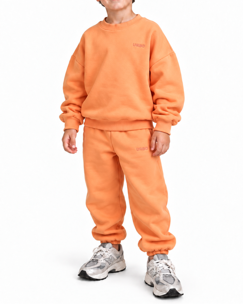 A young boy wearing a matching orange sweatshirt and sweatpants set, paired with gray sneakers, standing against a plain white background.