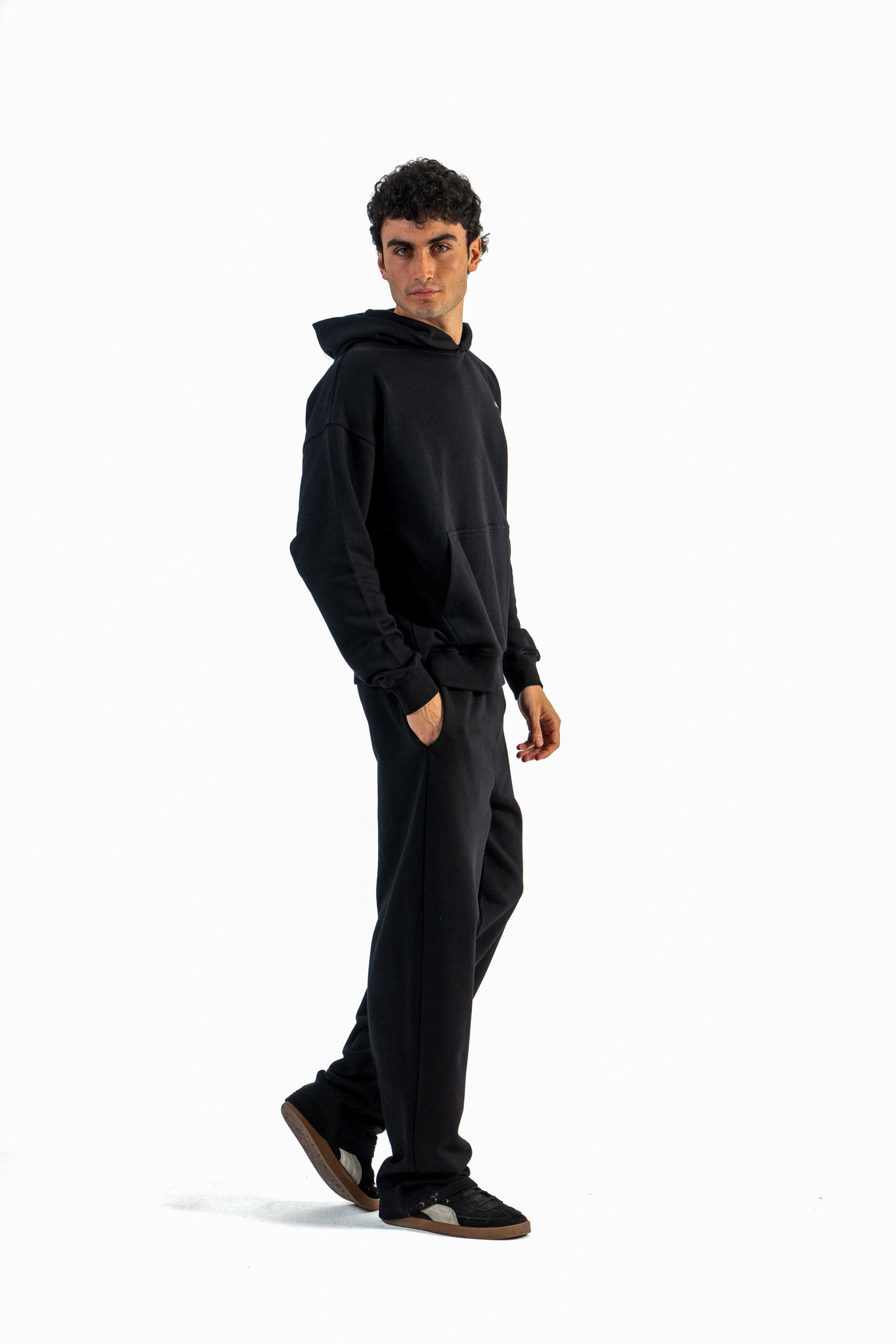 Person wearing a black hoodie and pants on a white background