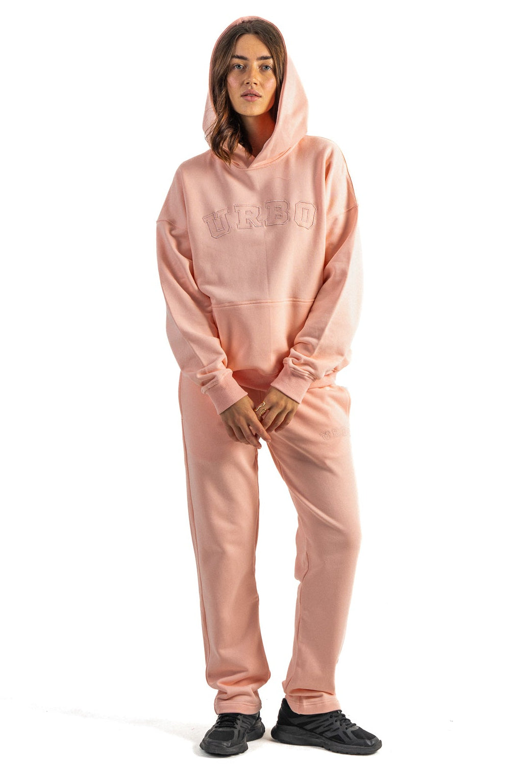 Person wearing a pink hoodie and pants set on a white background