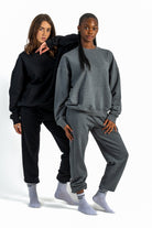Two people wearing matching black and gray sweatsuits on a white background