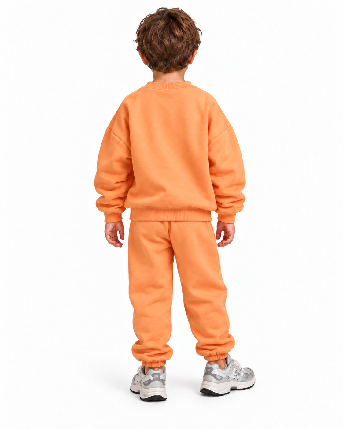 A child viewed from the back wearing a matching orange sweatshirt and sweatpants set with gray sneakers, photographed against a plain white studio background.