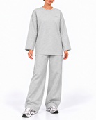 A woman modeling a light gray heathered lounge set consisting of a long-sleeve crewneck sweatshirt and matching wide-leg sweatpants, paired with silver sneakers, against a plain white studio background.