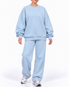 A model wearing a light blue sweatshirt and matching sweatpants set, paired with silver sneakers, against a plain white studio background.