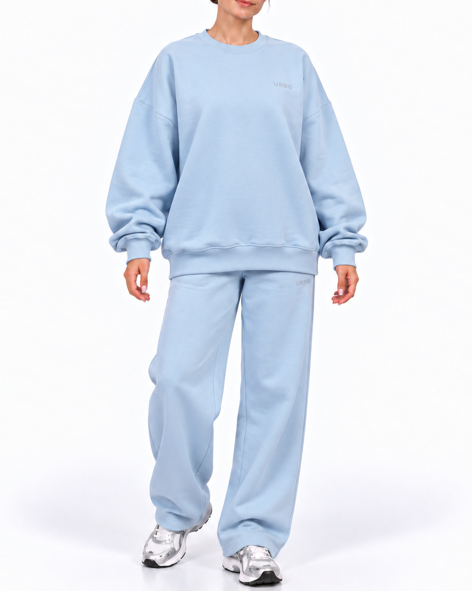 A model wearing a light blue sweatshirt and matching sweatpants set, paired with silver sneakers, against a plain white studio background.